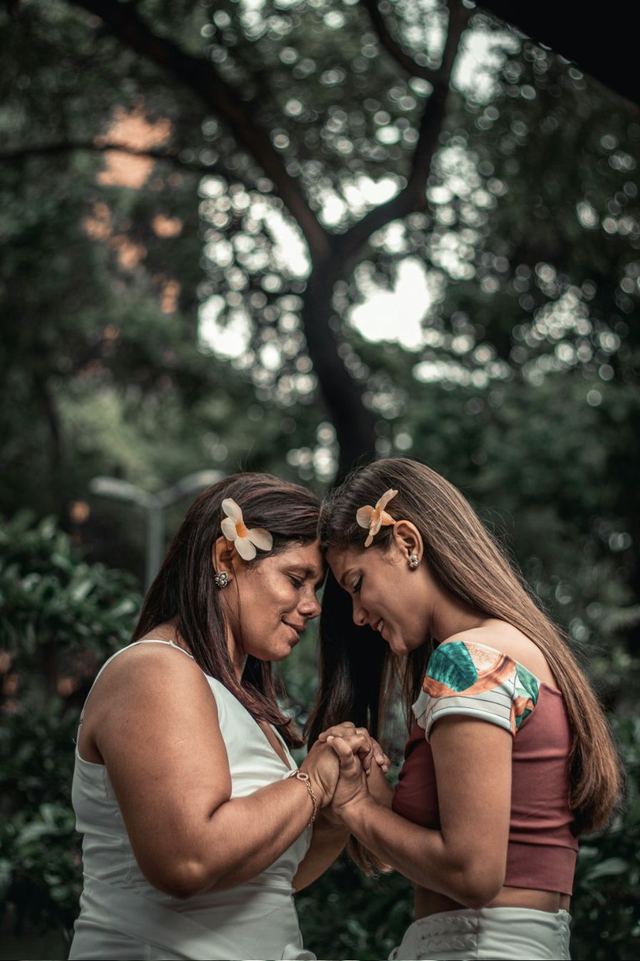 A mother and daughter touching foreheads and holding hands under a tree